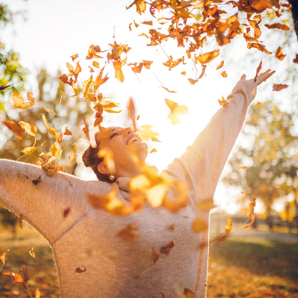 Woman throws autumn leaves into the air with joy
